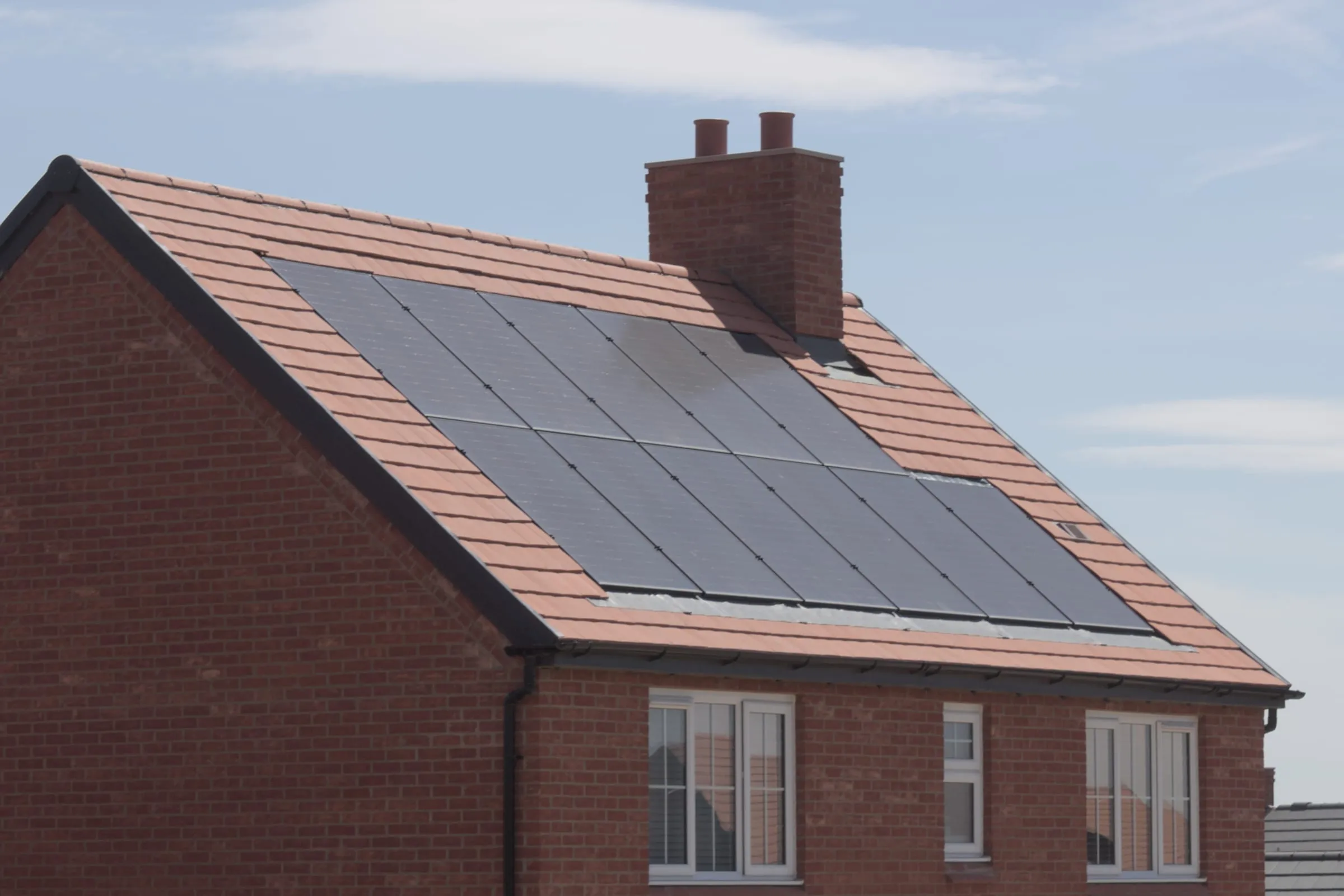 A black solar array set into the tiled roof of a red brick house against a clear sky.