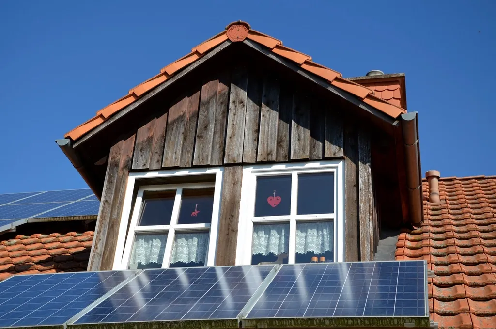 The timber gable of a house, with solar panels fitted across the pantile roof below its windows.